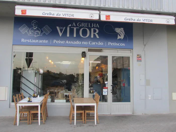 Fachada do restaurante com o letreiro A Grelha do Vítor e duas mesas à porta